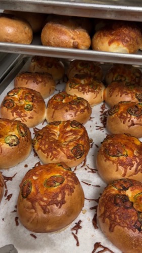 A sheet tray of fresh jalapeño cheddar bagels with baked cheddar and sliced jalapeño on top