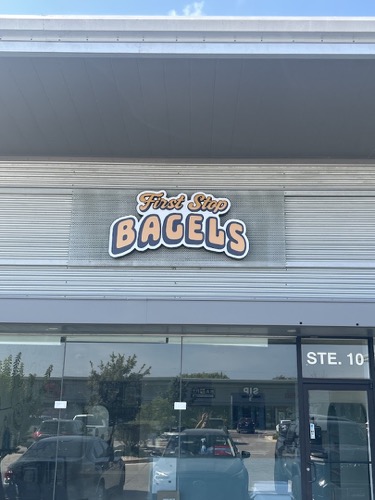 The First Stop Bagels storefront: the retro First Stop Bagels sign on grey corrugated metal above the glass door of Suite 10